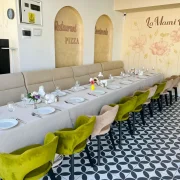 sala La Mami Acasa cu canapea, mese lungi si scaune verzi pe podea cu model geometric